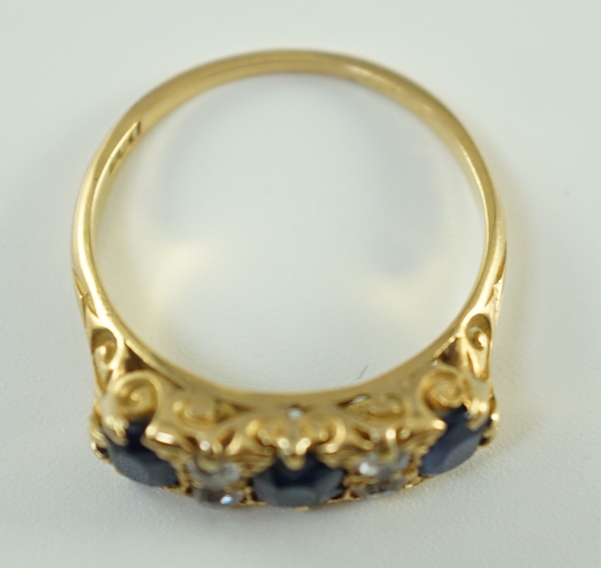 An early 20th century 18ct gold, three stone oval cut sapphire and four stone diamond spacer set half hoop ring